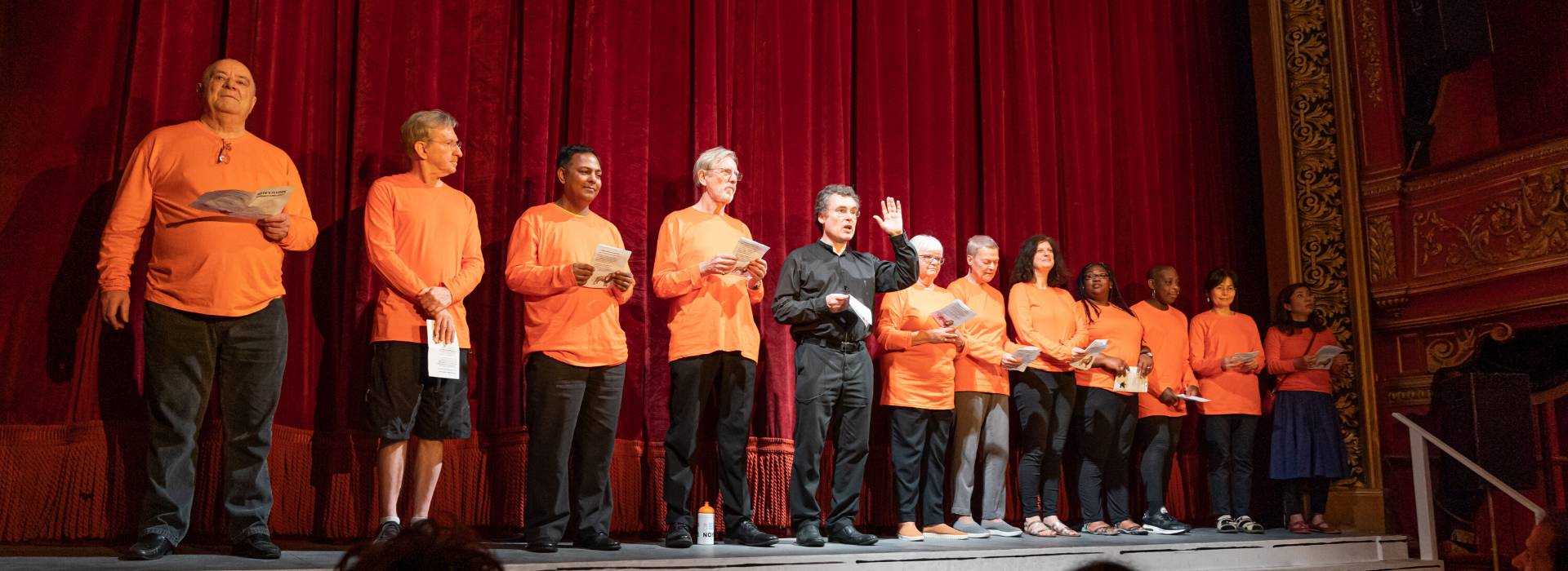 12 members of Stratford East's Newham Community Groups Programme. Many are wearing long-sleeved orange t-shirts. 