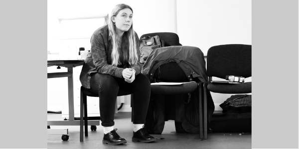 Photo of Grace Duggan. Grace sitting on a chair, with their arms resting on their legs.