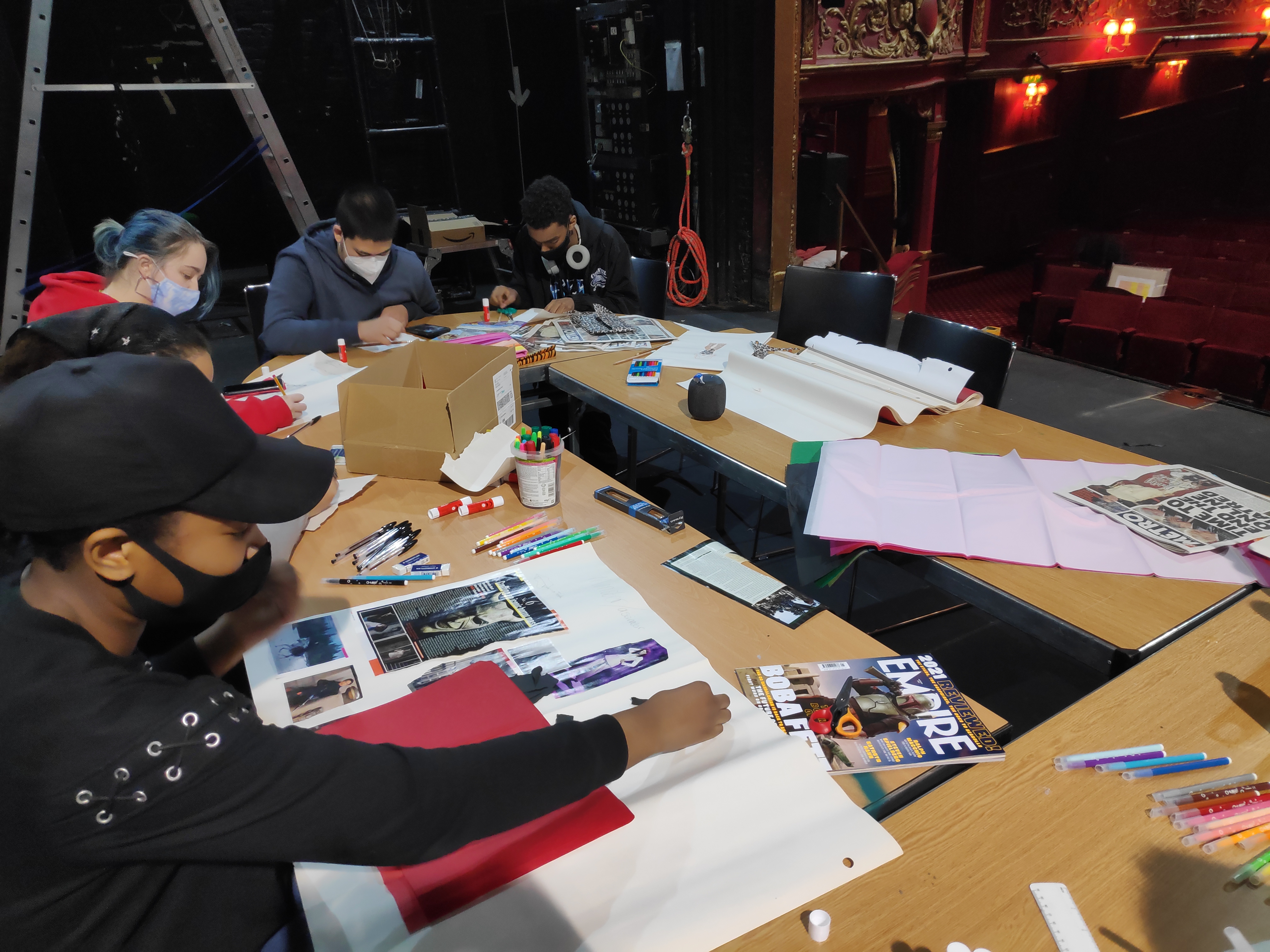 Group photo of Young Technicians sitting at a desk creating costume designs.